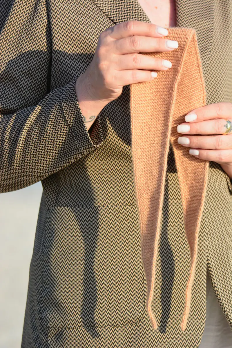 Il foulard aperto, tenuto tra le mani davanti a una giacca.